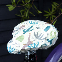 Load image into Gallery viewer, Say goodbye to plastic bags on bike seats in the rain! An original funny design with hand drawn succulent and cactus illustrations, this elasticated Desert in Bloom waterproof saddle cover is both pretty and functional. Size of cover: 23cm (width) x 24.5cm (length) One size fits all. Material: Card, Plastic, Elastic Dimensions: Length: 35 cm Height: 0.5 cm Width: 26.5 cm. Cyclists riders lovers gift idea.

